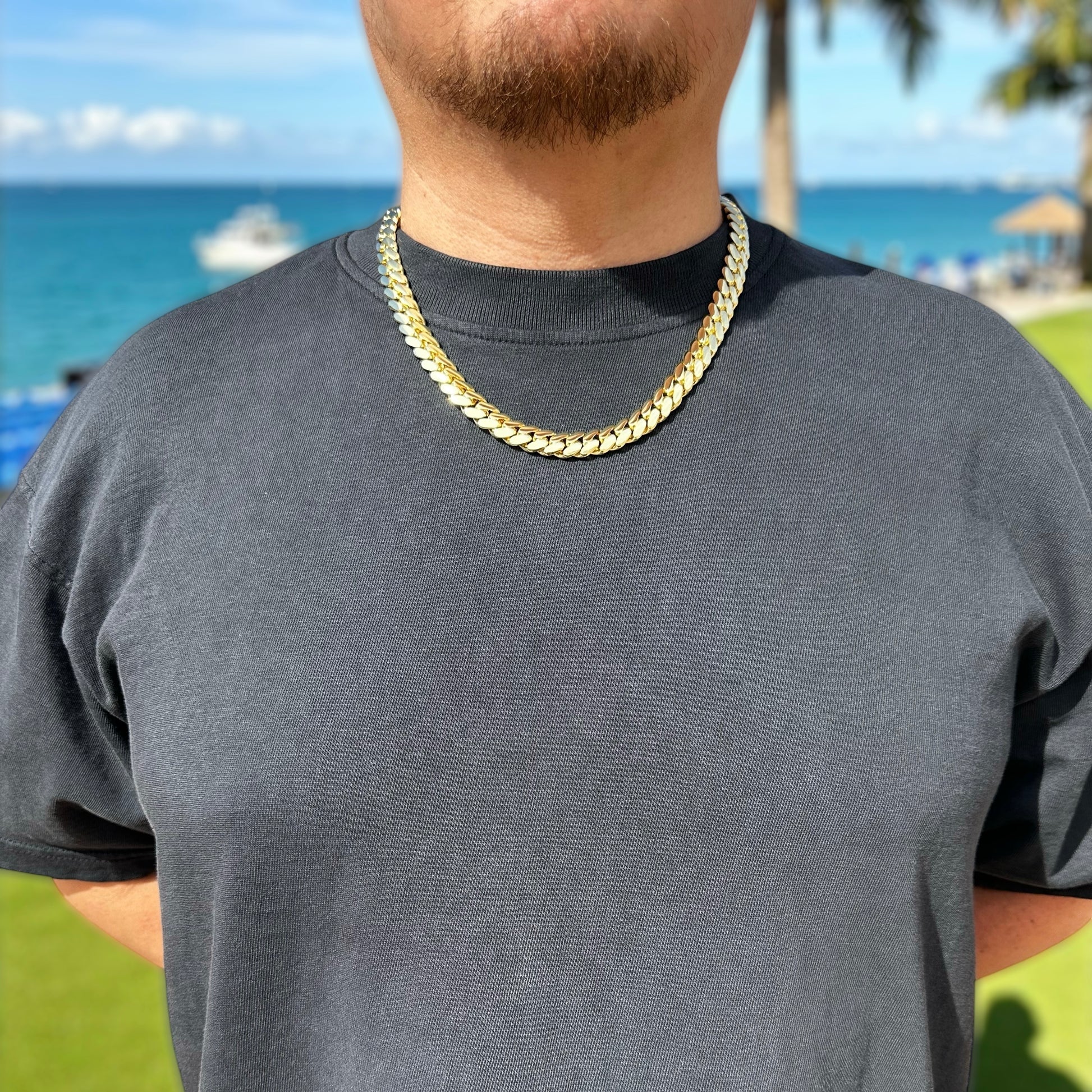 Person wearing a gold chain necklace with a beach in the background