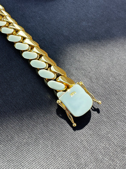 14K gold-plated Miami Cuban link bracelet with box clasp, polished finish, and secure side locks, displayed on dark fabric under natural sunlight.